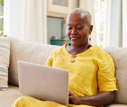 Attractive, smiling senior sitting on a sofa with her laptop open